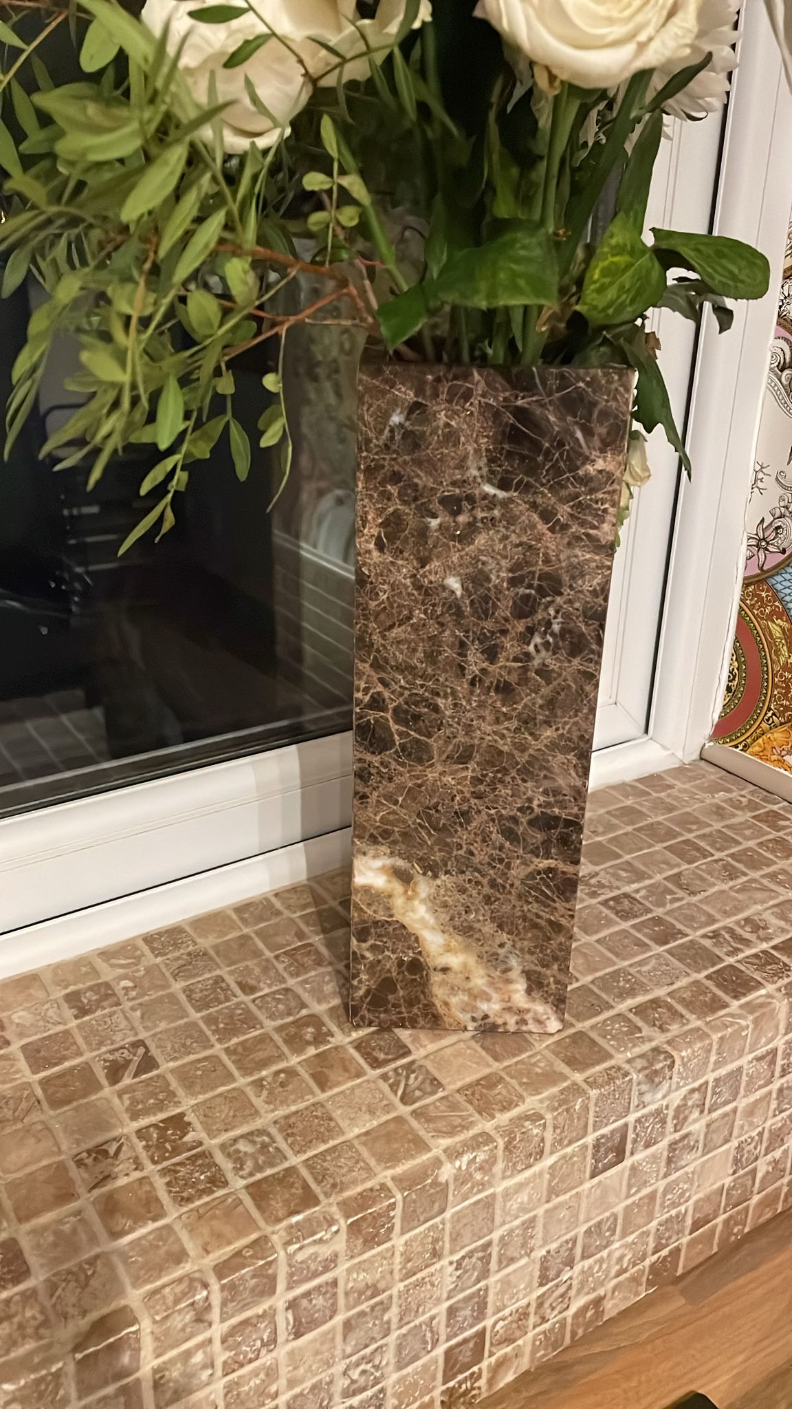 Marble tall bespoke vase in brown and dark marble with flowers on a window sill