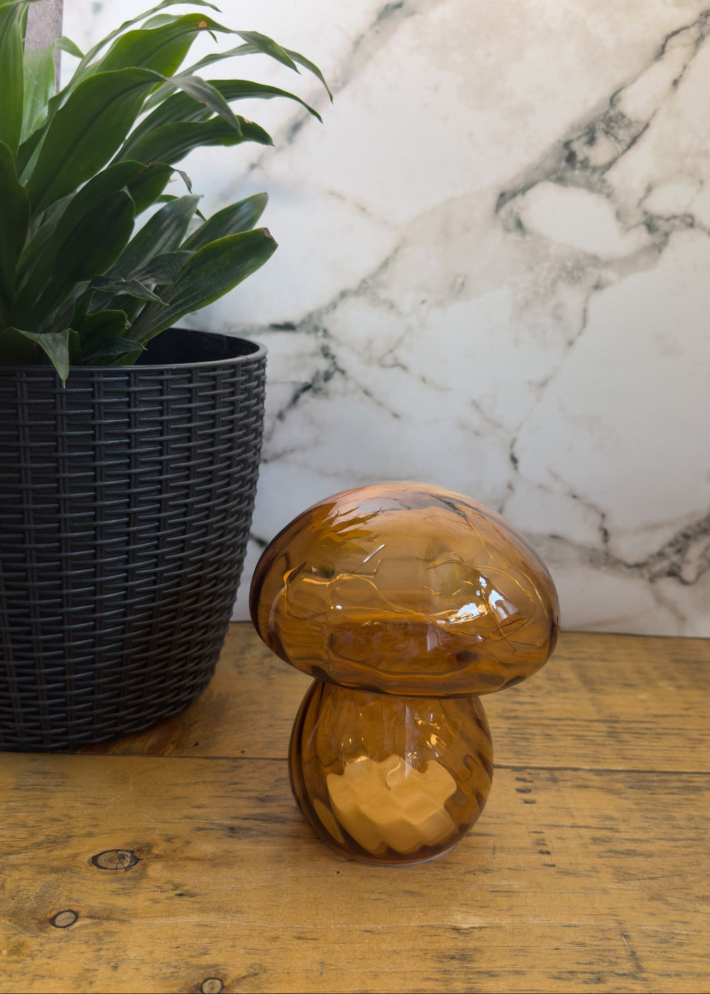 Amber /orange glass mushroom sculpture on a wooden surface with a marble wall in the background