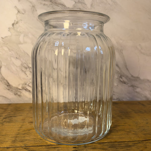 Clear glass jar on a wooden surface with a marble-patterned wall in the background