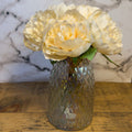 Decorative glass vase with white flowers on a wooden surface with a marble background
